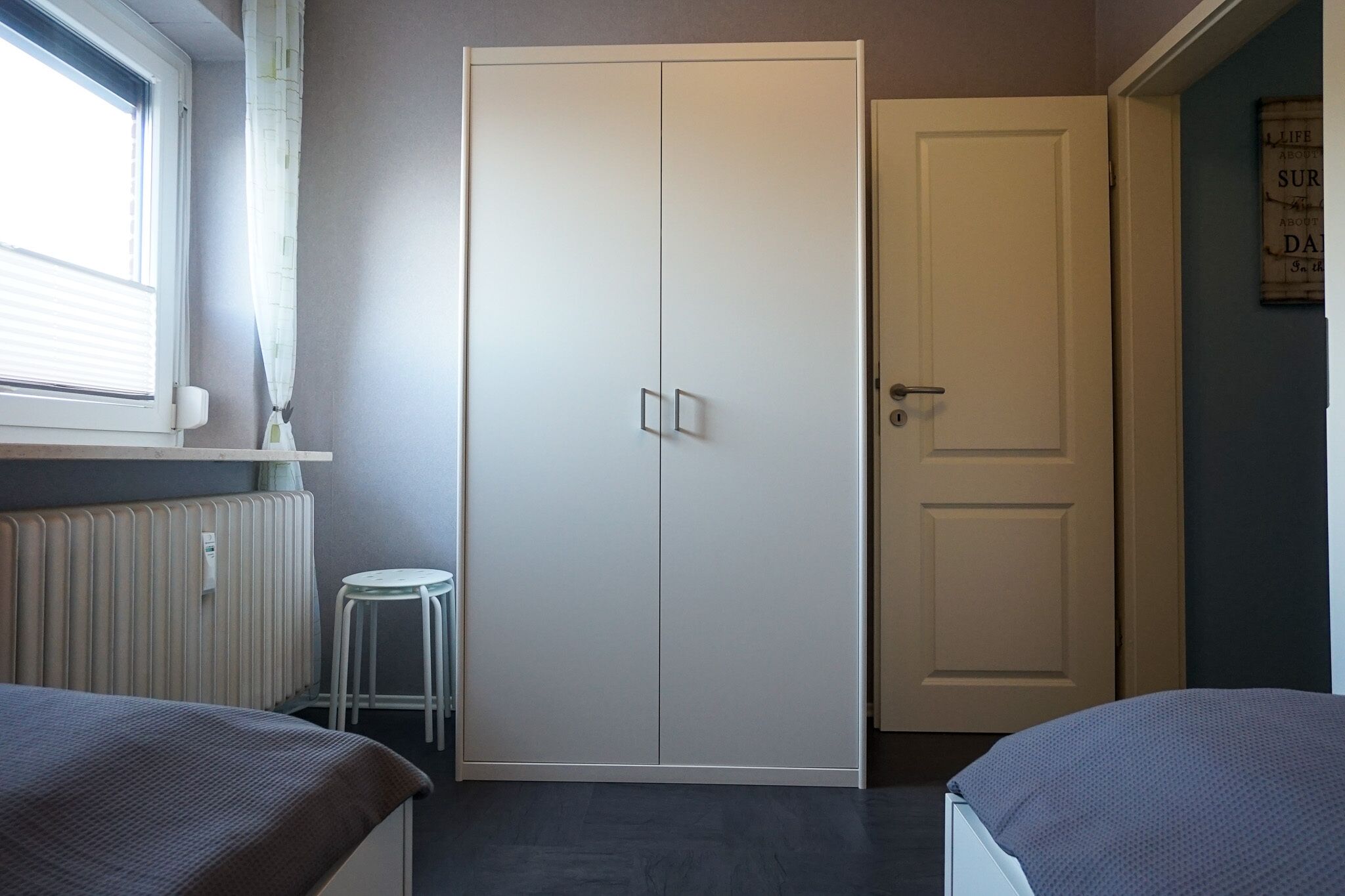 A bedroom with a bed, a radiator, a white wardrobe, and a door.