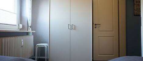 A bedroom with a bed, a radiator, a white wardrobe, and a door.