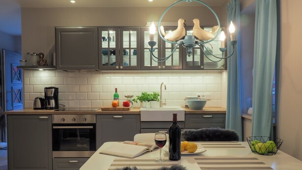 Cozinha moderna com armários cinza, bancada branca e uma área de jantar com mesa posta para dois.
