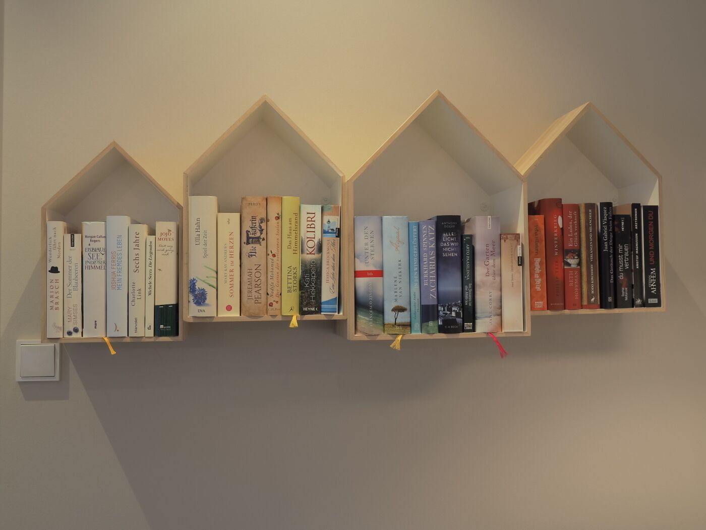 Three wooden bookshelves against a wall, each filled with books of various sizes and colors.