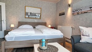 Hotelkamer met een houten bed, twee nachtkastjes, een witte nachtkast, een radiator, een aan de muur bevestigd schilderij en een ingelijste kunstwerk boven het bed.