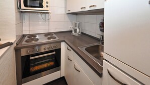 Een kleine keuken met een fornuis, oven, magnetron, koffiezetapparaat en een koelkast.