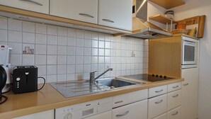 Et moderne køkken med hvide skabe, en Bosch opvaskemaskine, en vask og en mikrobølgeovn.