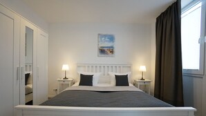 A neatly arranged bedroom with a bed, bedside tables, and a window with curtains. - Wohnung Deich Mitten in Büsum (Büsum)