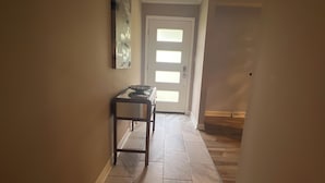 A hallway with a tiled floor, a door with frosted glass panels, and a small table with a bowl and a candle. - Convenient Location-Private watch the sun come up over a beautiful pasture (Greer)