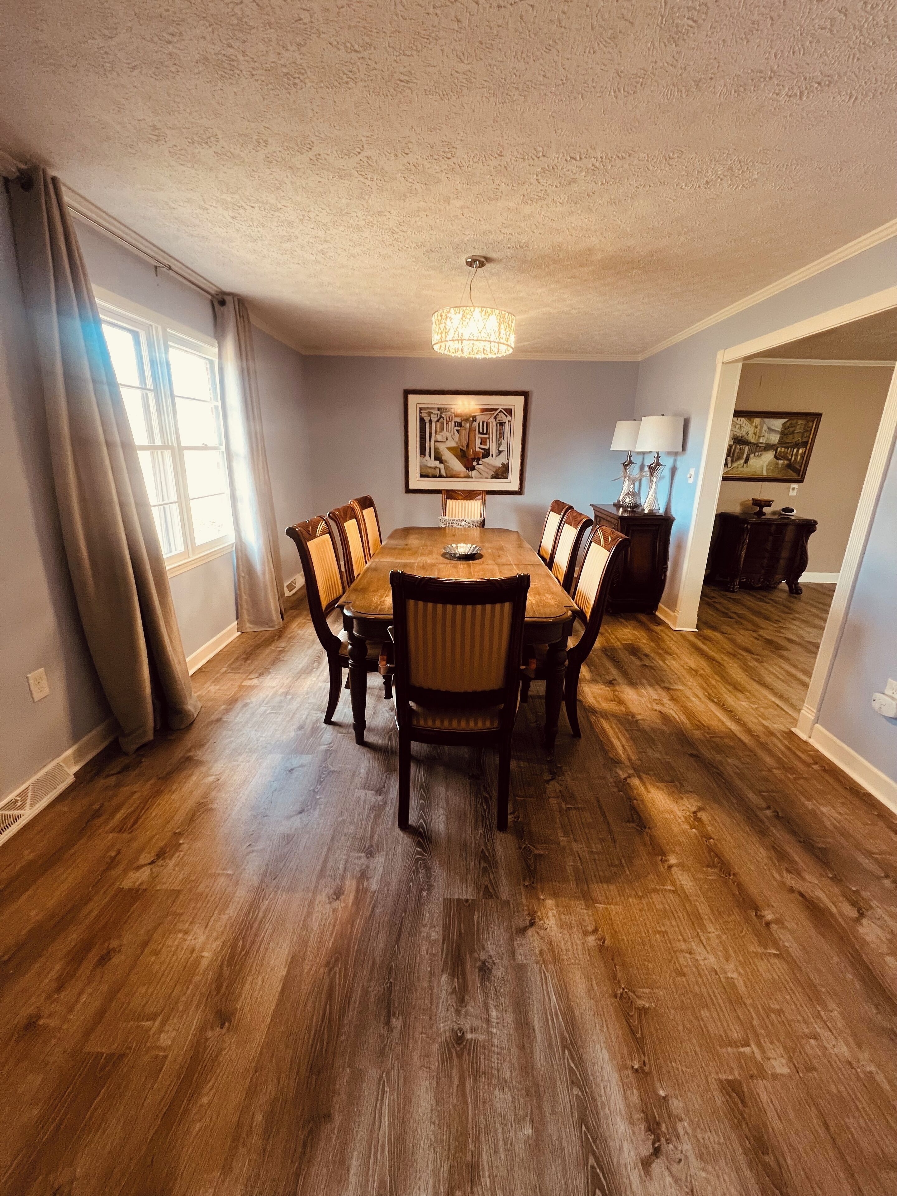 Une salle à manger avec une table et des chaises en bois, un lustre et des œuvres d’art accrochées au mur.