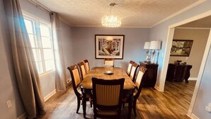 A dining room with a wooden table and chairs, a chandelier, and artwork on the wall. - Convenient Location-Private watch the sun come up over a beautiful pasture (Greer)