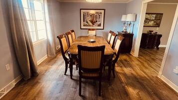 Une salle à manger avec une table et des chaises en bois, un lustre et des œuvres d’art accrochées au mur.