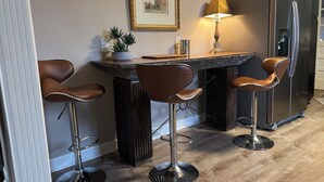 Et moderne køkken med en central ø, barstole, et køleskab og en hængende lampe.
