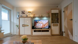 Een woonkamer met een televisie, houten kasten, een open haard en een eethoek met een schaal bloemen.