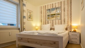 Een slaapkamer met een houten bed, een raam met zonwering, een nachtkastje met een lamp, en een muur met gestreept behang en ingelijste foto's.