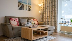 Een gezellige woonkamer met een bank, een houten bijzettafeltje en uitzicht op de omgeving door grote ramen.