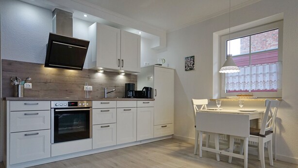 Una cocina moderna con armarios blancos, horno empotrado y comedor con mesa y sillas.