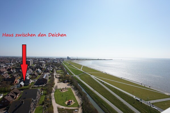 Luchtbeeld van een kustplaatsje met een gemarkeerd huis tussen twee groene zones.