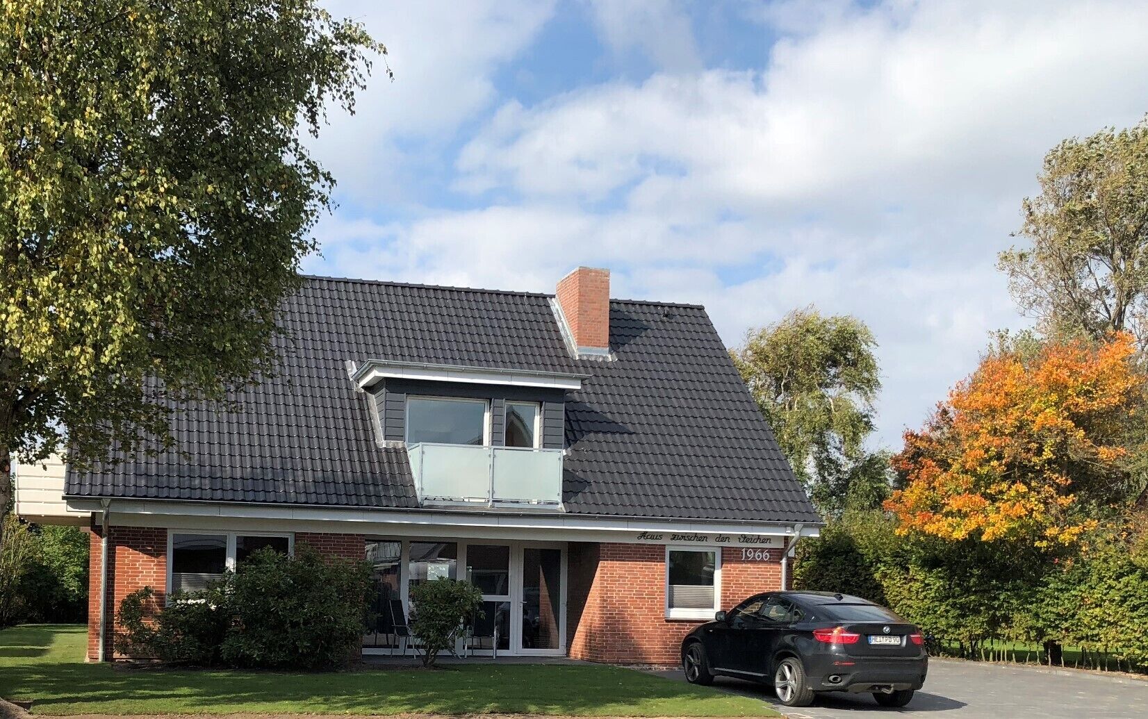 A two-story house with a dark roof, a visible attic window, and a brick facade.