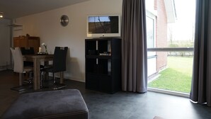 Una sala de estar moderna con comedor, un televisor de pantalla plana y un amplio ventanal con cortinas.