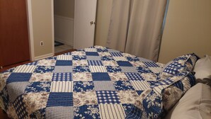 Ein Schlafzimmer mit einem Bett, das mit einer blau-weißen Quilts überzogen ist, einer Holztür und einer weißen Wand.