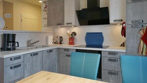 A modern kitchen with grey cabinets, a black microwave, and a blue chair. - Wohnung Helios im Herzen von Büsum (Büsum)