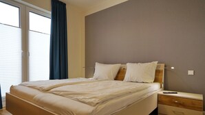 A bedroom with a bed, a nightstand, and a window with curtains. - Wohnung Helios im Herzen von Büsum (Büsum)