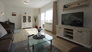 Ett modernt vardagsrum med ett soffbord i glas, en soffa, en tv på ett träställ och ett vitt skåp.