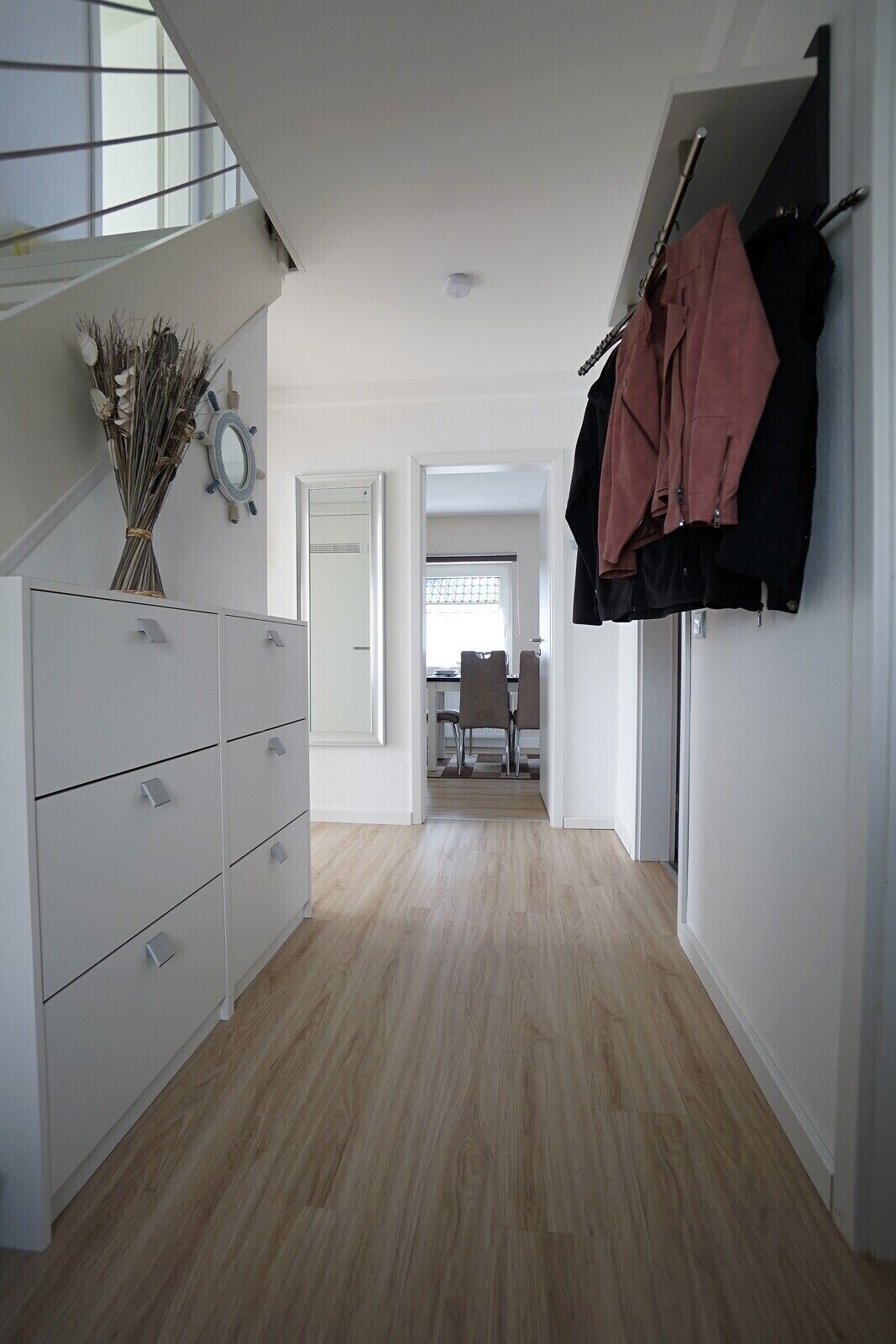 A modern, well-lit hallway with a wooden floor, white cabinetry, and a mirror on the wall.