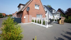 Ett bostadshus med en fasad av tegel, en satellitantenn och ett vitt staket med inslag av grönska.