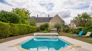 Une piscine rectangulaire dotée d’une terrasse carrelée, entourée de haies et d’arbres bien entretenus.