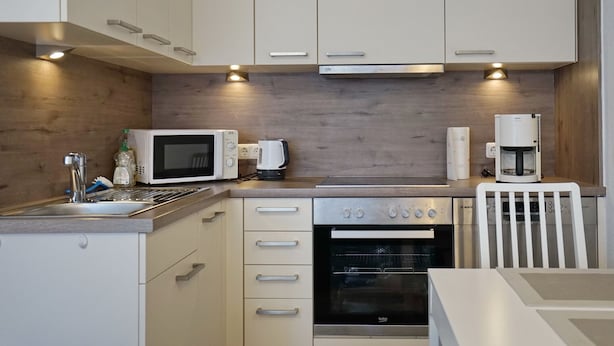 Una cocina moderna con armarios blancos, microondas, cafetera y horno.