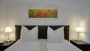 Habitación de hotel con una cama doble, dos mesitas de noche con lámparas y un cuadro colgado en la pared que muestra un campo lleno de flores.