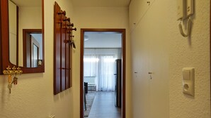 Un pasillo estrecho con suelo de madera, una puerta al final que da a una habitación con radiador y un teléfono en la pared.