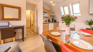 A modern kitchen with wooden cabinets, a dining area with a wooden table set for two, and a large mirror on the wall. - Le City-Break - T3 en centre-ville avec un parking sécurisé (Vannes)