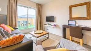 A living room with a sofa, a coffee table, a TV, and a desk with a computer. - Le City-Break - T3 en centre-ville avec un parking sécurisé (Vannes)
