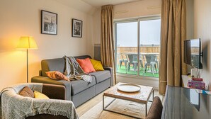 A living room with a sofa, a coffee table, a TV, and a balcony with chairs. - Le City-Break - T3 en centre-ville avec un parking sécurisé (Vannes)