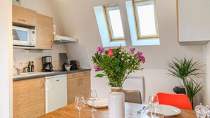 A modern kitchen with wooden cabinets, a built-in oven, and a dining area with a wooden table set for two. - Le City-Break - T3 en centre-ville avec un parking sécurisé (Vannes)