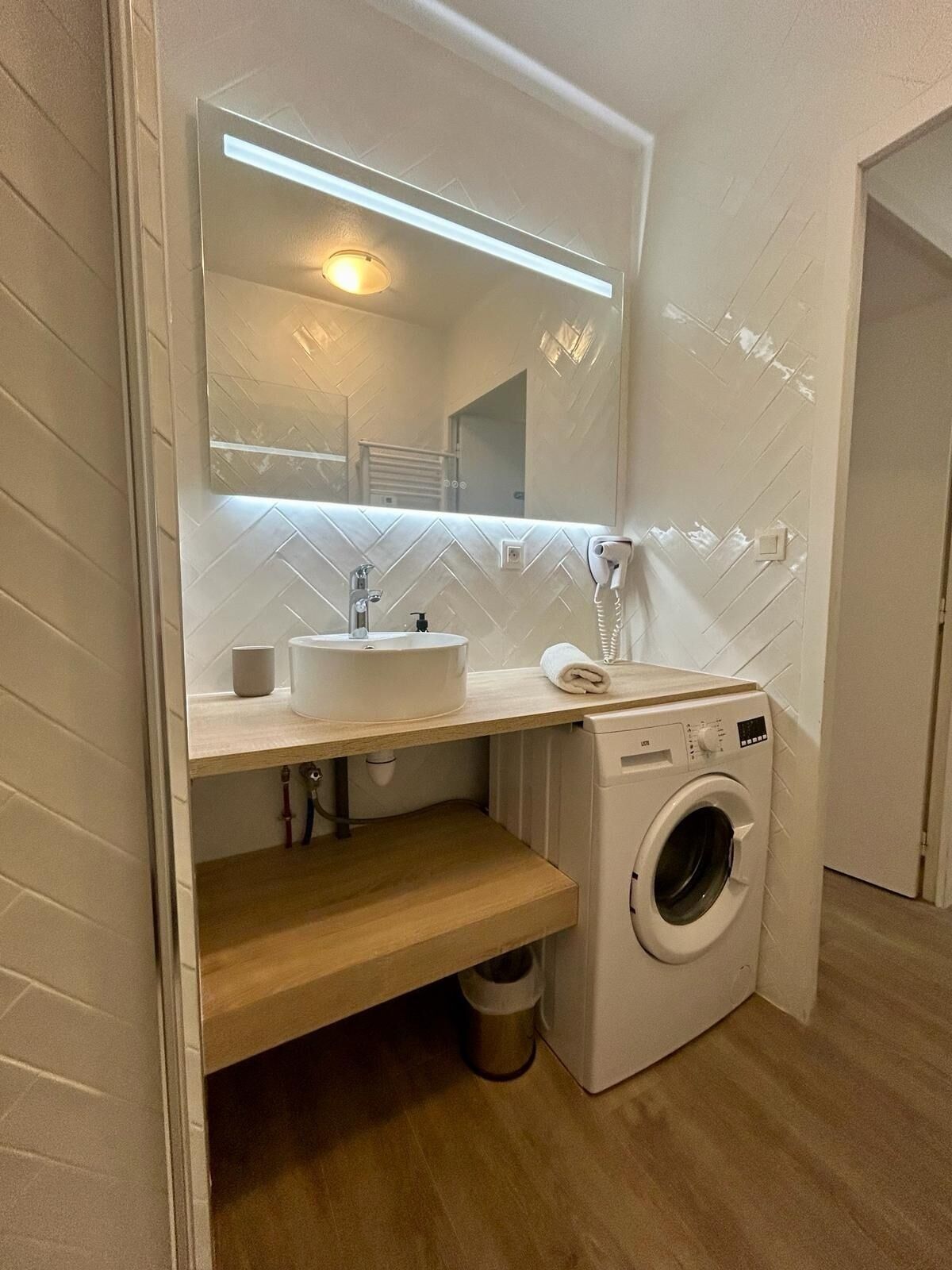Een kleine badkamer met een wastafel, spiegel en wasmachine.