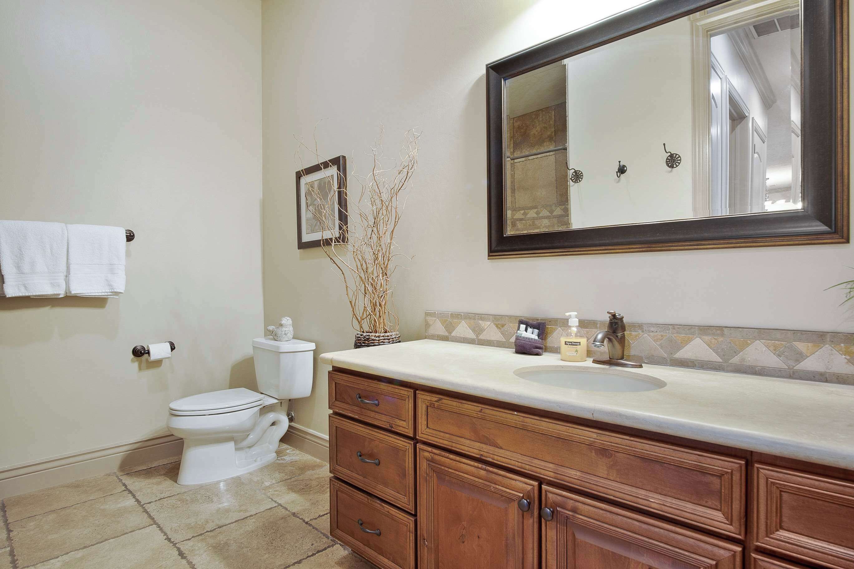 A bathroom with a toilet, sink, vanity, and mirror.