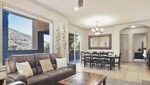 A living room with a leather sofa, a wooden coffee table, and a dining area with a chandelier. - Sierra Sky Patio w/ Fireplace (Hurricane)