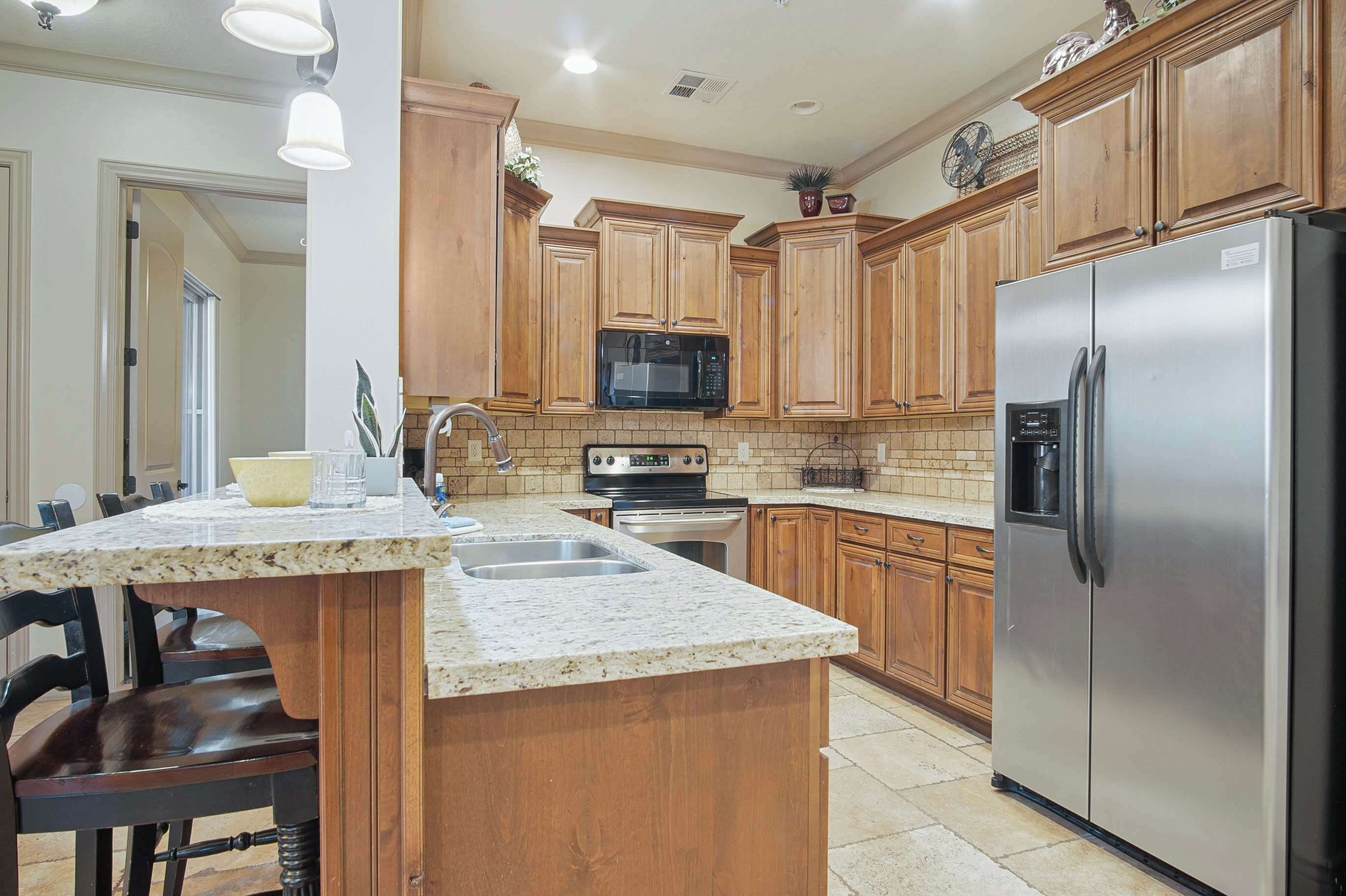 A kitchen with wooden cabinets, a stainless steel refrigerator, a microwave, and a granite countertop.