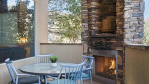 An outdoor patio with a stone fireplace, a round glass table, and blue chairs. - Sierra Sky Patio w/ Fireplace (Hurricane)