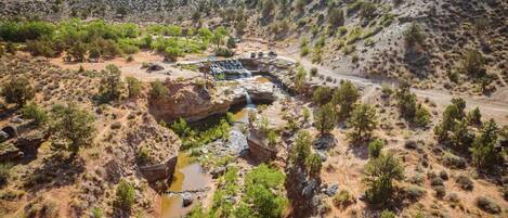 A natural landscape with a waterfall, rocky terrain, sparse vegetation, and a dirt road.