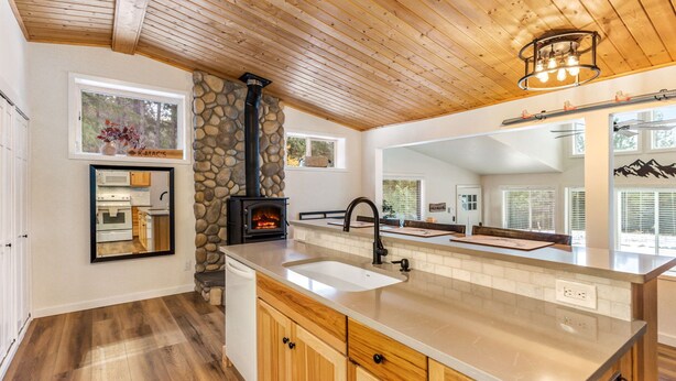 A modern kitchen with a stone fireplace, wooden cabinets, and a large island with a sink.