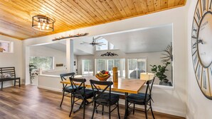 A dining area with a wooden ceiling, a large wall clock, and a view of the outdoors through large windows.