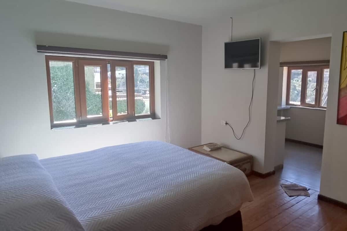 Un dormitorio con una cama grande, un televisor montado en la pared y una ventana con vistas a zonas verdes.