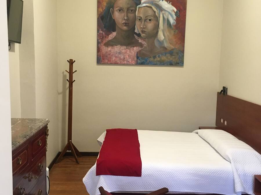 A bedroom with a bed, a wooden dresser, a chair, and a painting on the wall.