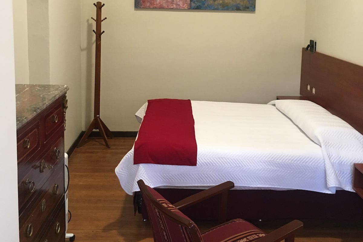 Un dormitorio con una cama, un aparador de madera, una silla y un cuadro en la pared.