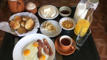 A breakfast tray with eggs, bacon, biscuits, cheese, cereal, jam, and orange juice.