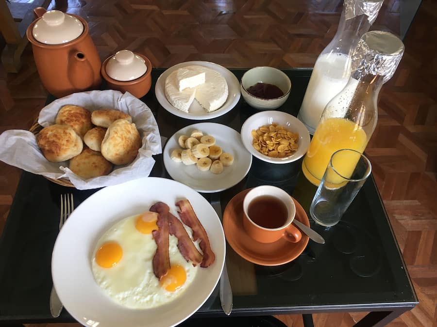 A breakfast tray with eggs, bacon, biscuits, cheese, cereal, jam, and orange juice.
