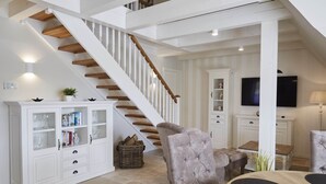 A spacious living area with a wooden staircase, a television, and a dining table. - Traumhafter Urlaub Unter Reet - Reethus "de Tweeling" Apartment OG (Büsum)