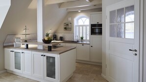 A kitchen with white cabinetry, a central island, and a large window. - Traumhafter Urlaub Unter Reet - Reethus "de Tweeling" Apartment OG (Büsum)