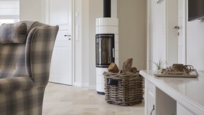 A living room with a plaid armchair, a white fireplace, and a wicker basket with logs. - Dreamlike vacation under thatch - Reethus "de Tweeling" Apartment ground floor (Büsum)